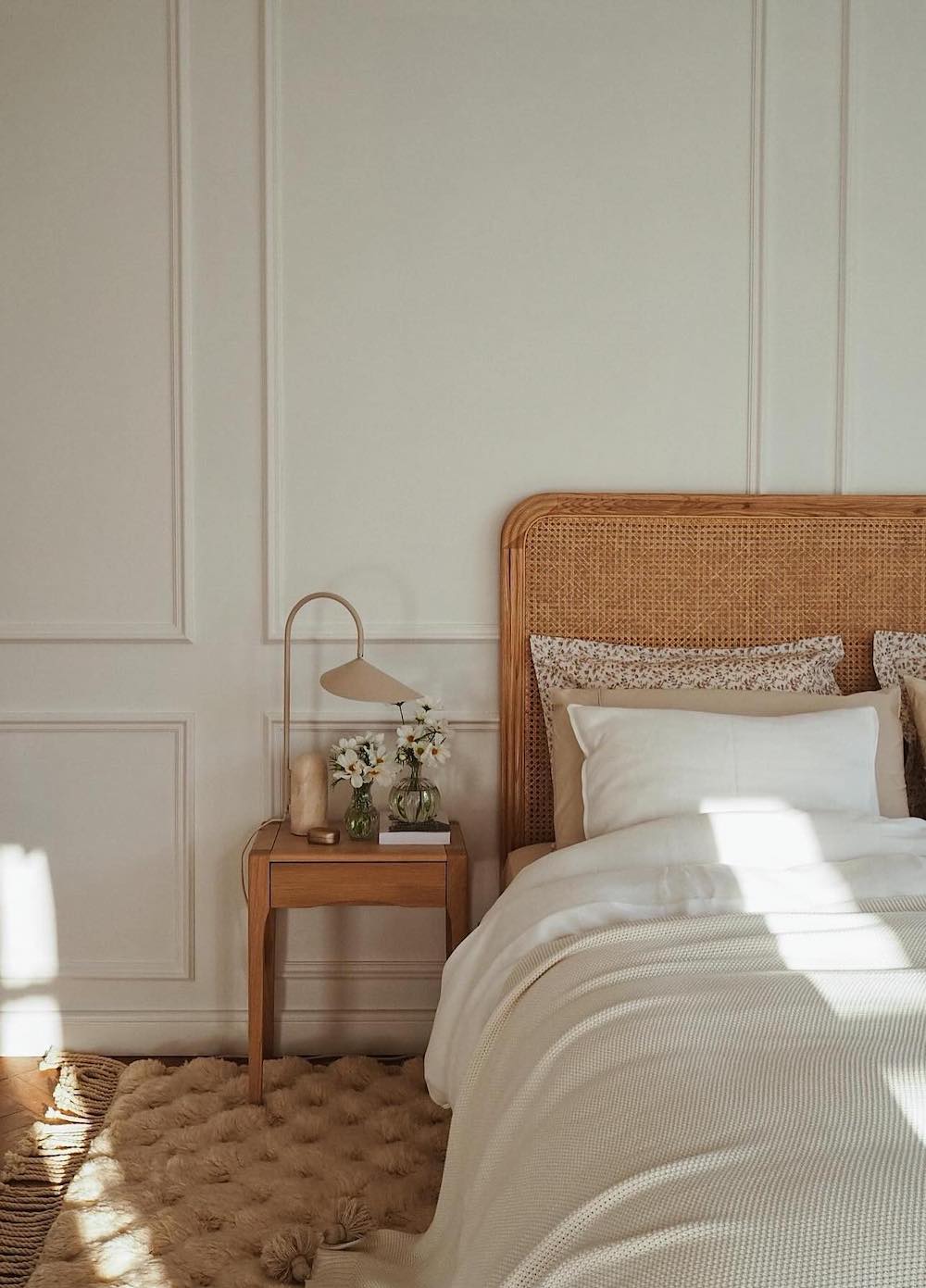 a bohemian-inspired minimalist bedroom with a rattan headboard, floral decor, and earthy tones