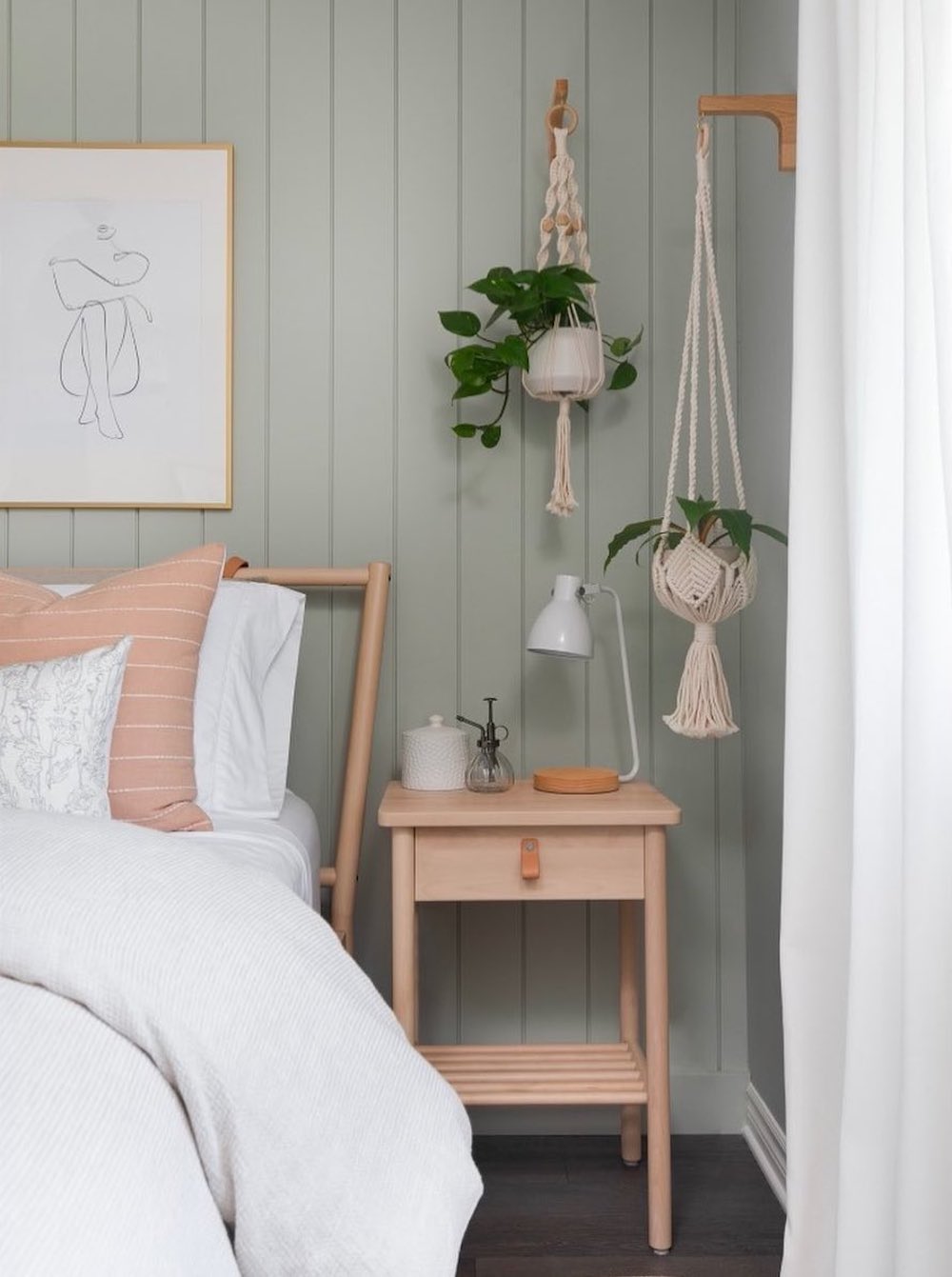 a boho bedroom with soft green board and batten walls, ivory and pink bedding, natural wood, and real plants