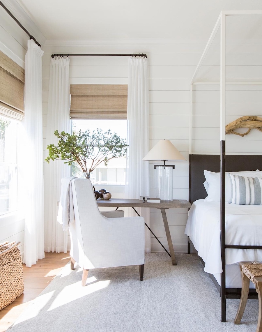 a white and beige coastal bedroom with a large bed frame, a lounging chair, and natural elements