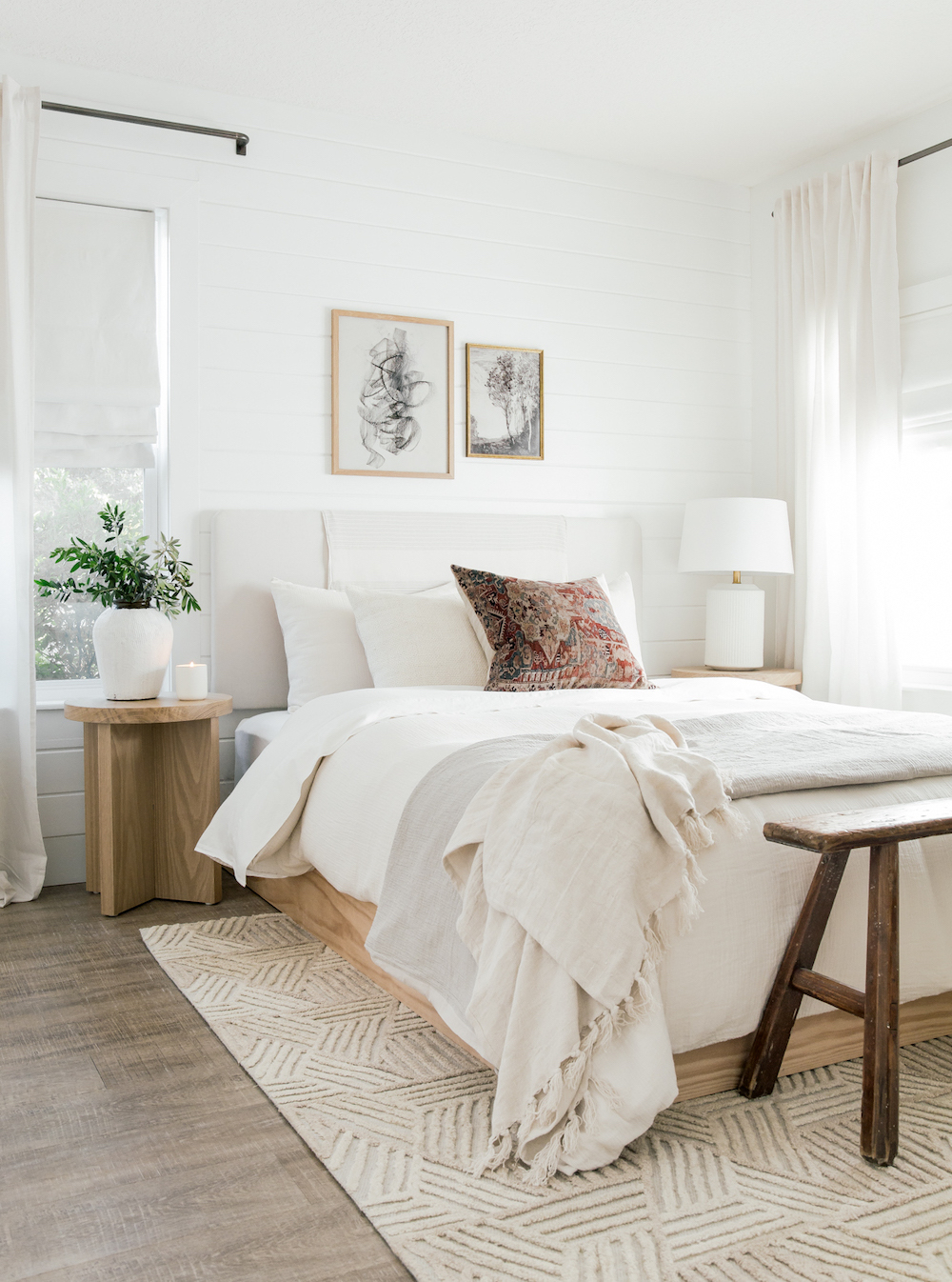 a bedroom with white bedding, statement pillows and art, and a textured rug