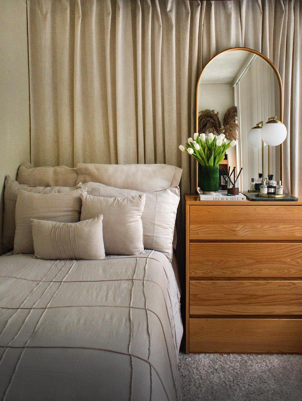 a bedroom with beige bedding and a warm wooden dresser