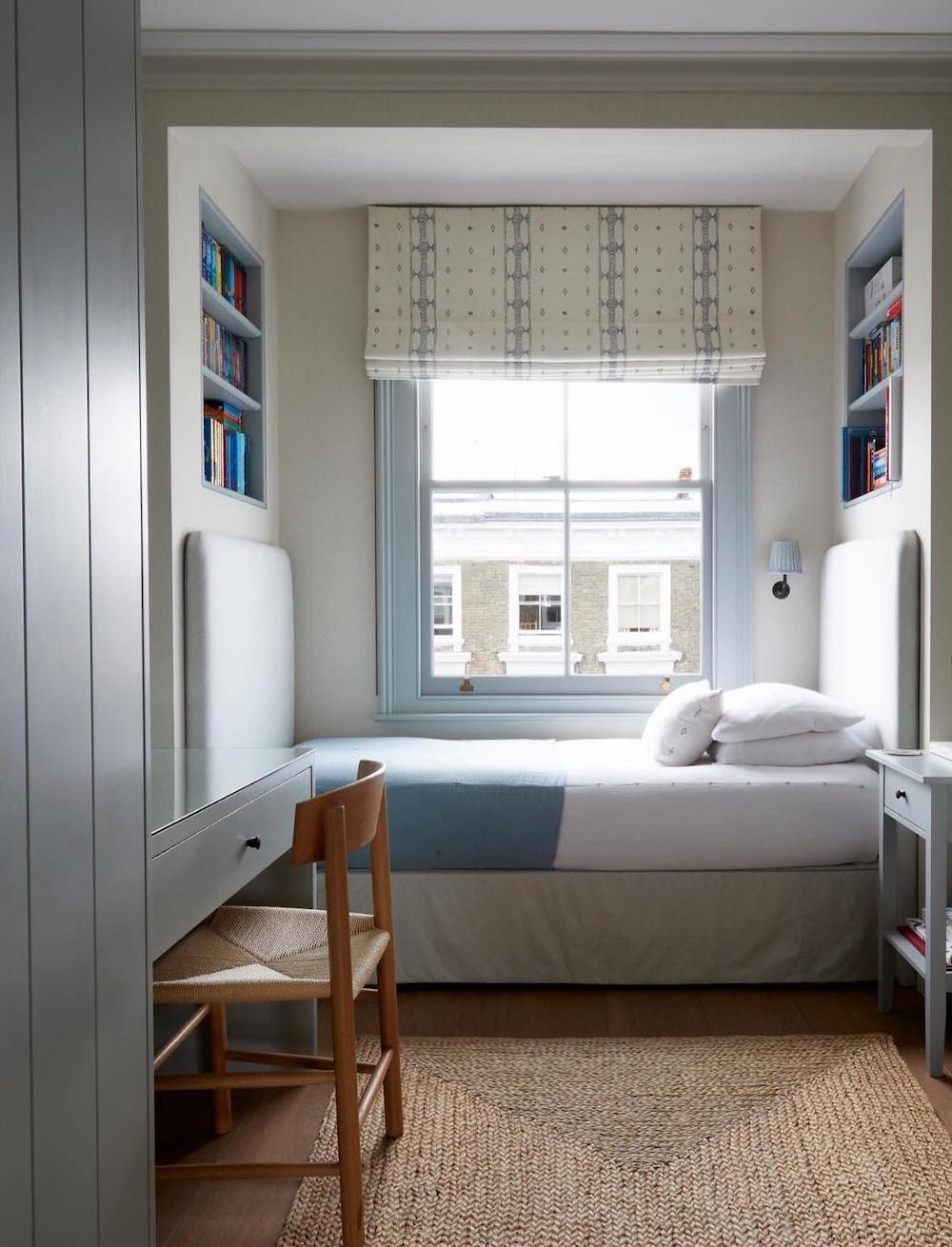 a white and baby blue bedding, bookshelves on either side of the bed, and a desk