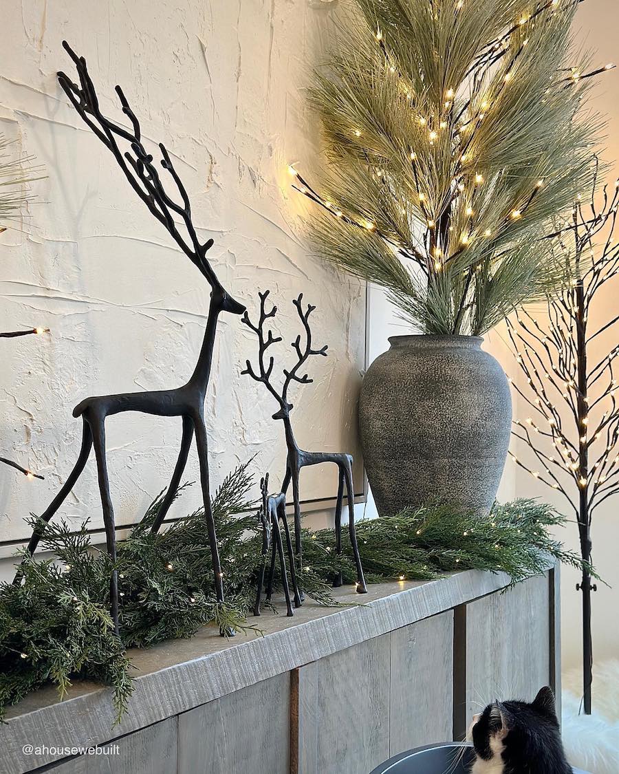 indoor christmas decor with black reindeer, pine garland, and a pine arrangement in a stone vase