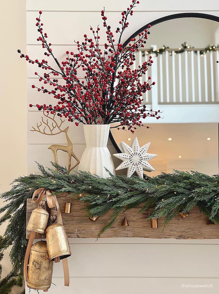 a mantle with holly berries, reindeer decor, bells, and pine garland