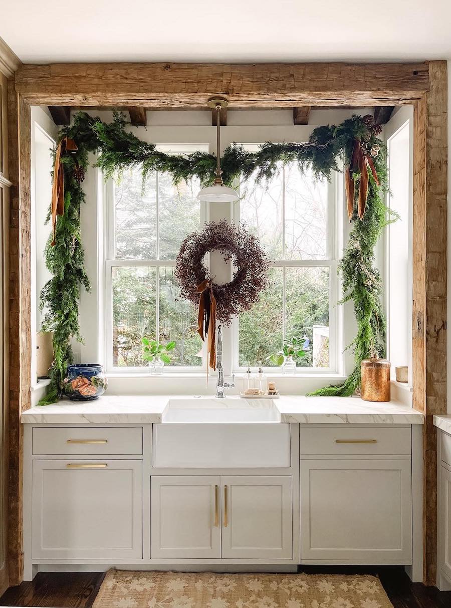 a kitchen sink with a winter wreath and pine garland