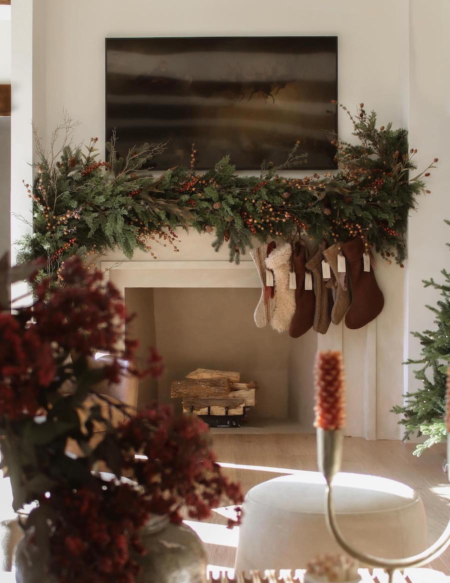 a fireplace with a large berry filled pine garland and stockings