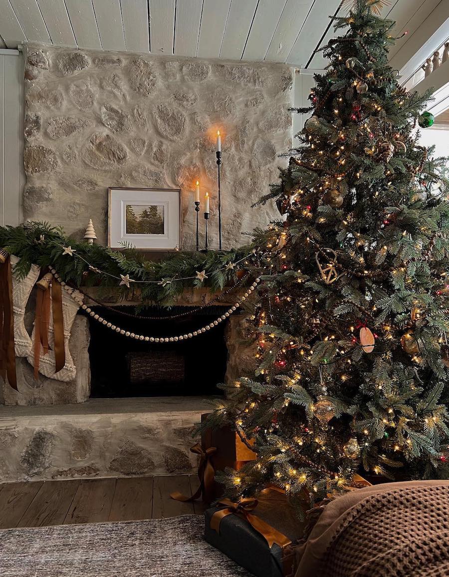 a living room with a large christmas tree, pine, wooden bead, and star garland, lit candles, and stockings