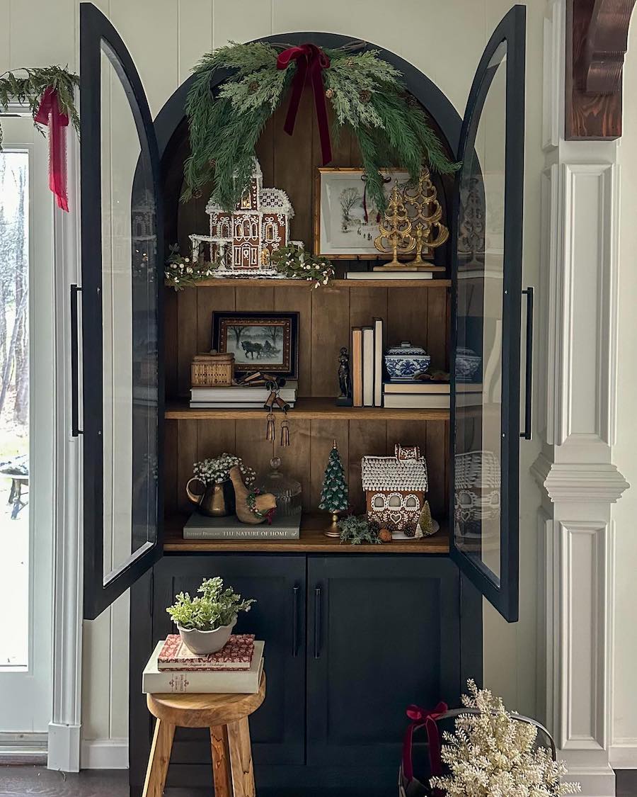 a black hutch with a gingerbread houses, pine decor, and red ribbons