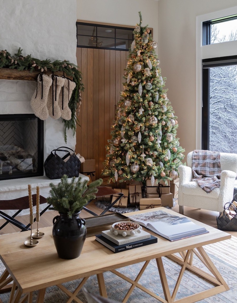 a living room with a white and gold decorated christmas tree, shearling stockings, and pine garland