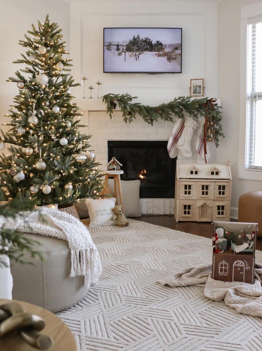 a living room with a small tree, knit blankets, a gingerbread doll house, and stockings