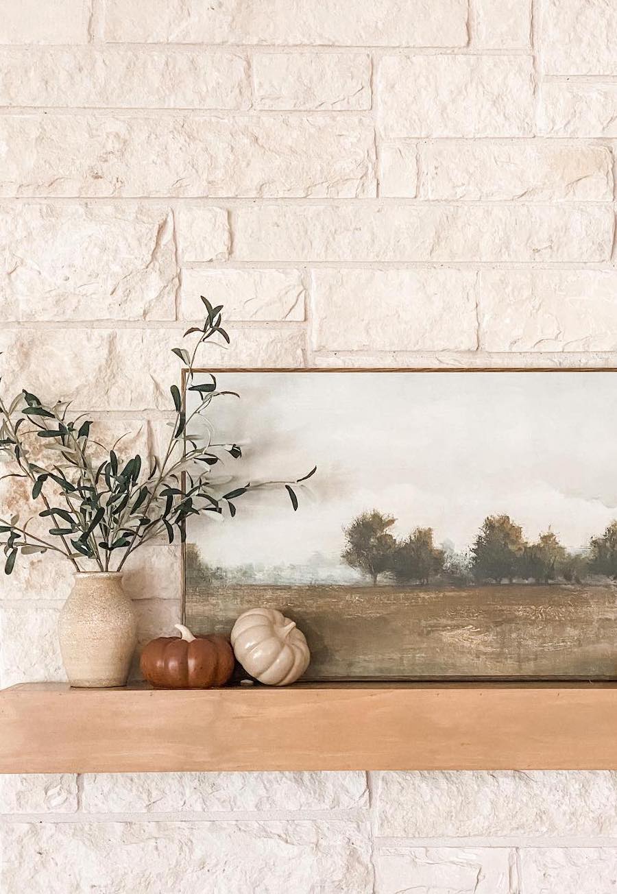 a vintage landscape art print, leaf bouquet, and ceramic pumpkins on a wooden floating shelf