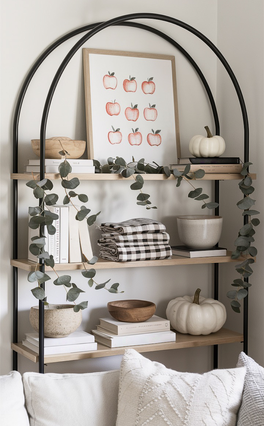 a living room shelf with an apple art print, plaid linens, white pumpkins, and eucalyptus accents