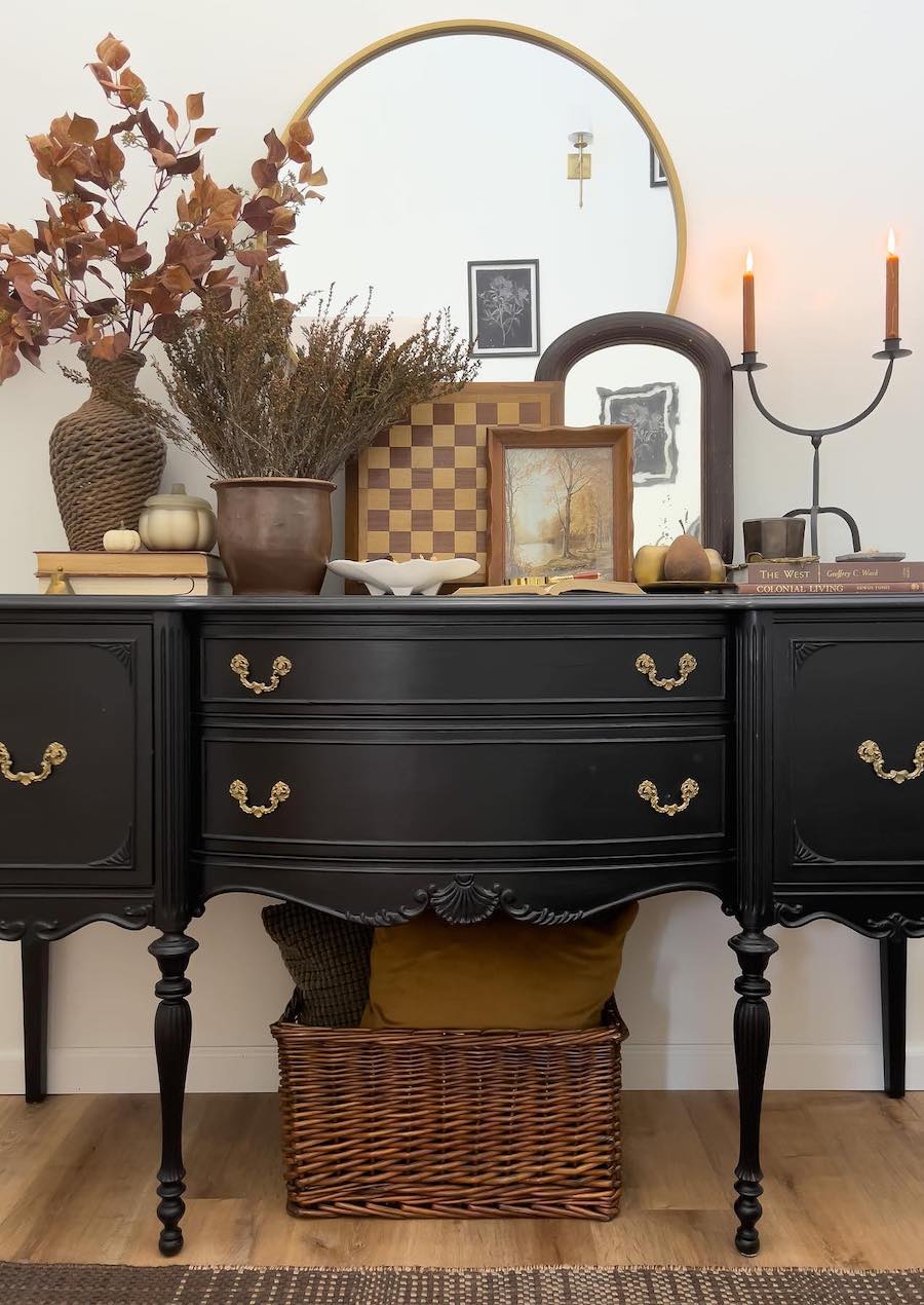 a black entryway table featuring antique autumn-inspired decor like fall foliage bouquets, candles, and pumpkins