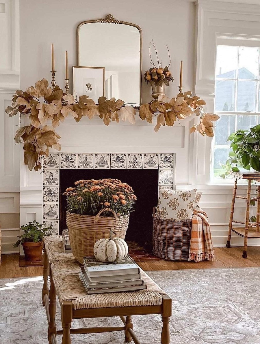 a farmhouse style living featuring a fall foliage garland, autumn bouquets, pumpkins, and fall-inspired pillows and blankets