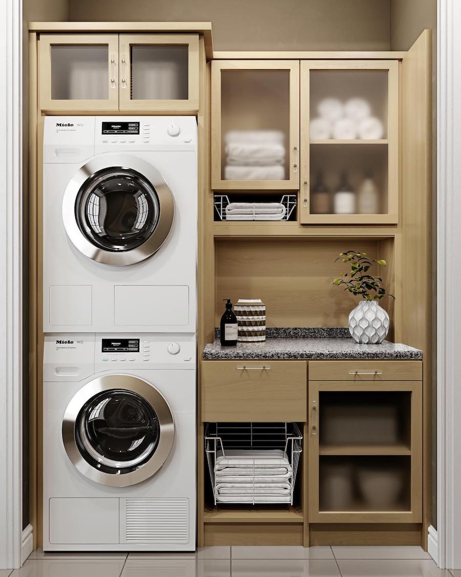 stacked washing and drying machines with a small counter, cabinets, and drawers surrounding them