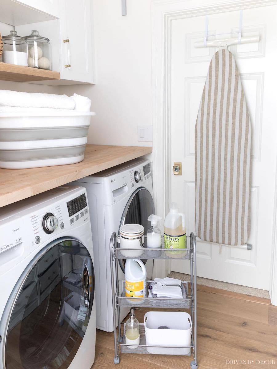 a laundry room with a rolling cart, wooden counter, and other storage