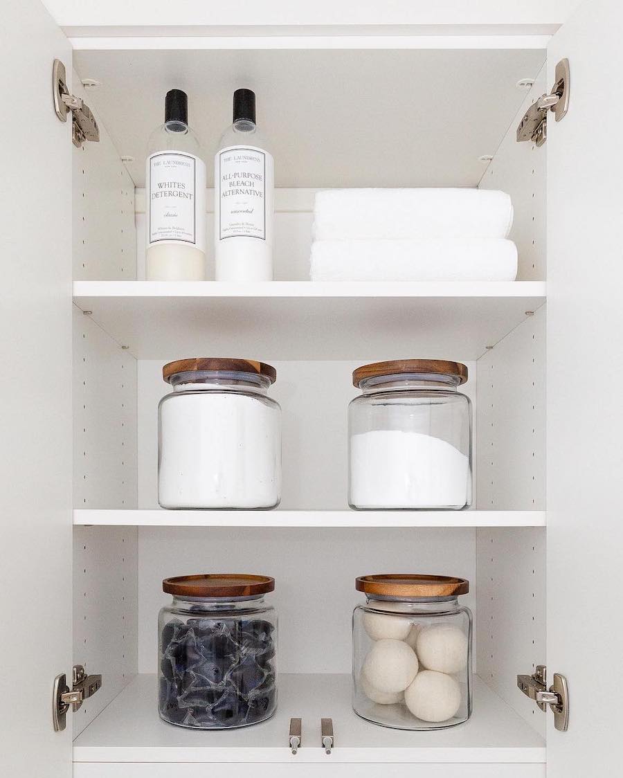 a laundry room shelf with glass canisters containing wool balls, laundry pods, and oxygen powder