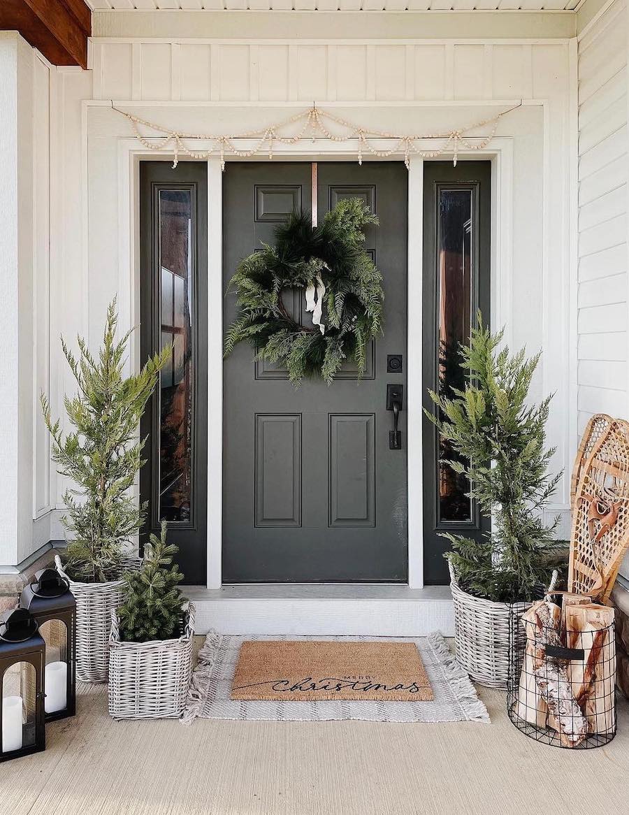 a front porch with outdoor christmas decor including small pine trees, lanterns, wreaths, and wooden snow shoes