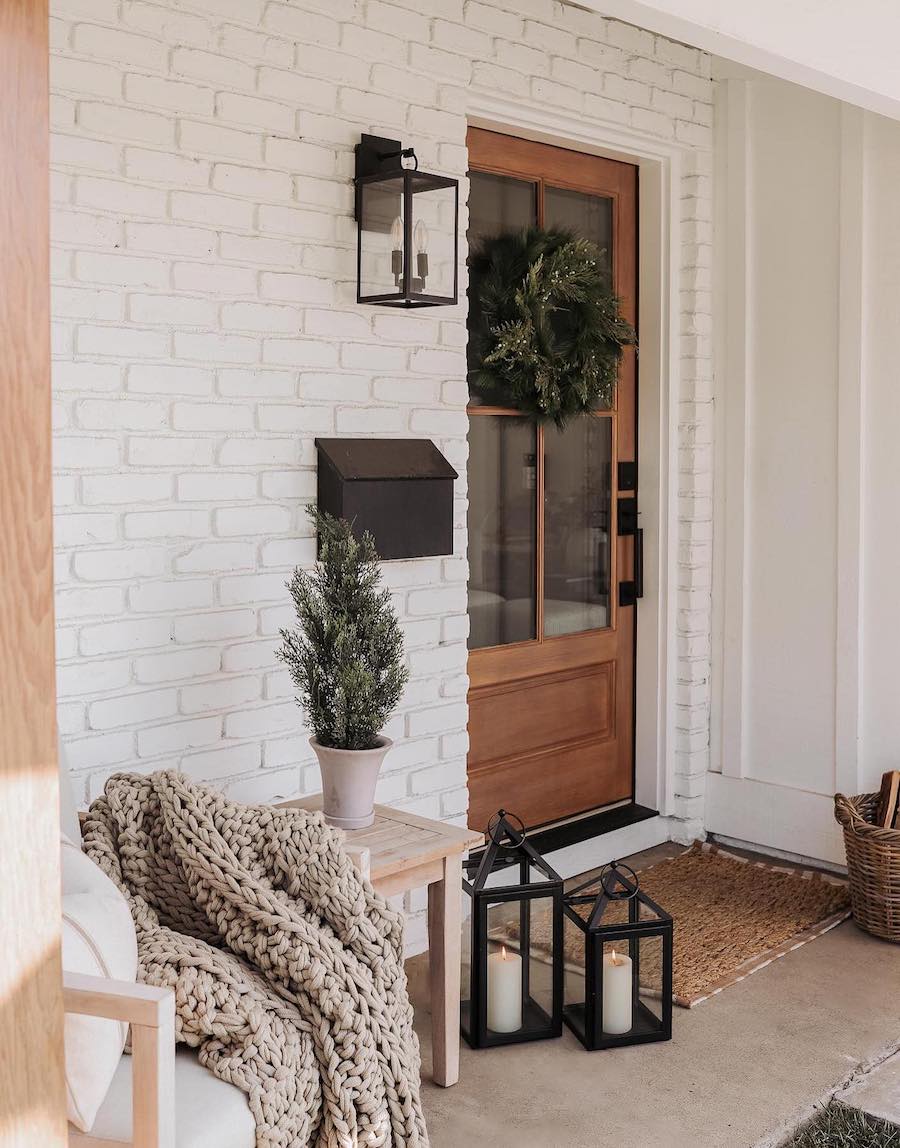 a front porch with lanterns, knit throw blankets, and pine decor