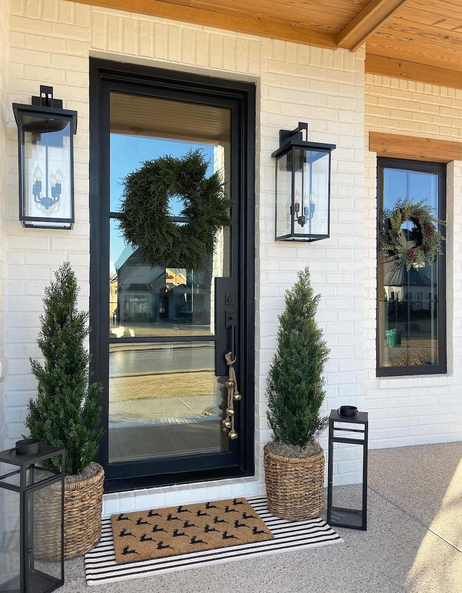 a front porch featuring pine trees, a wreath, and lanterns