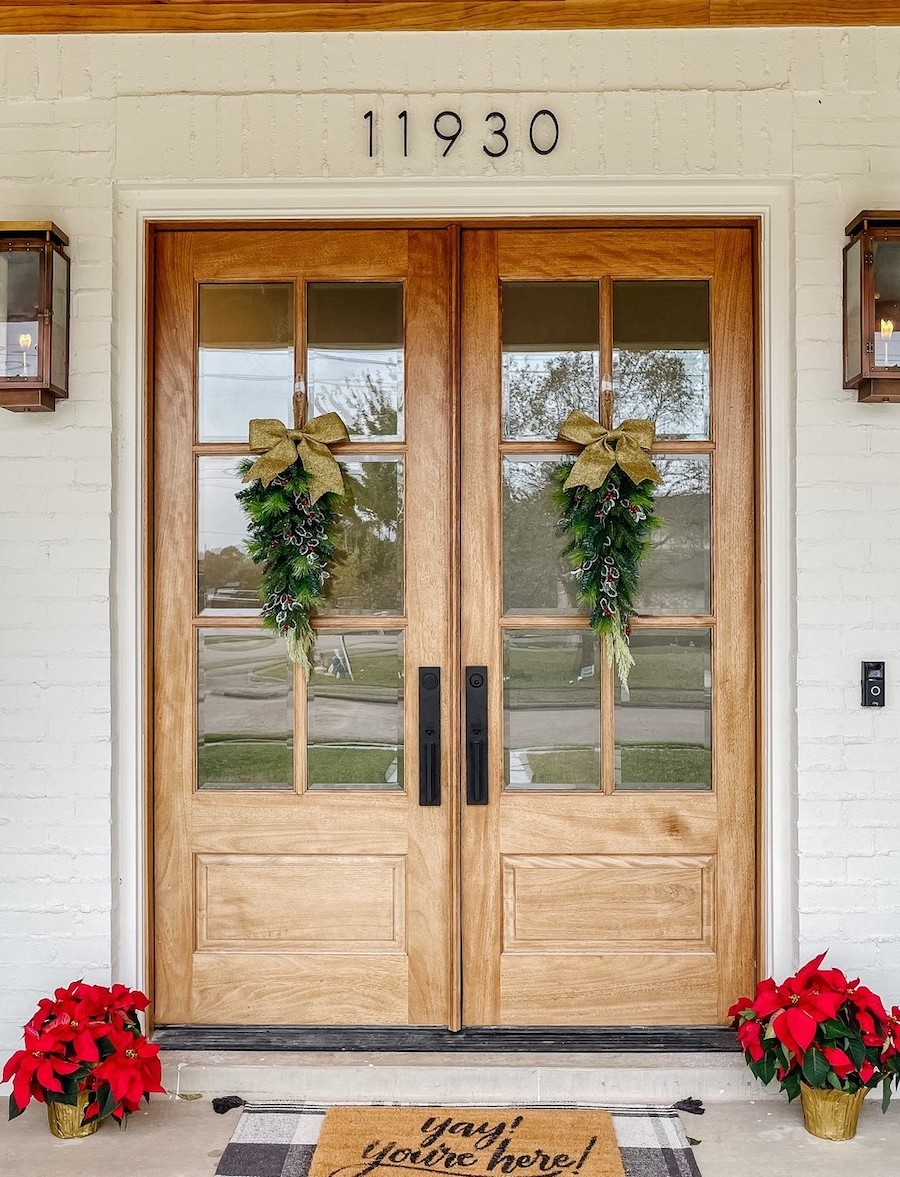 a front porch featuring wooden doors with gold bows and pine decor, and red poinsettias