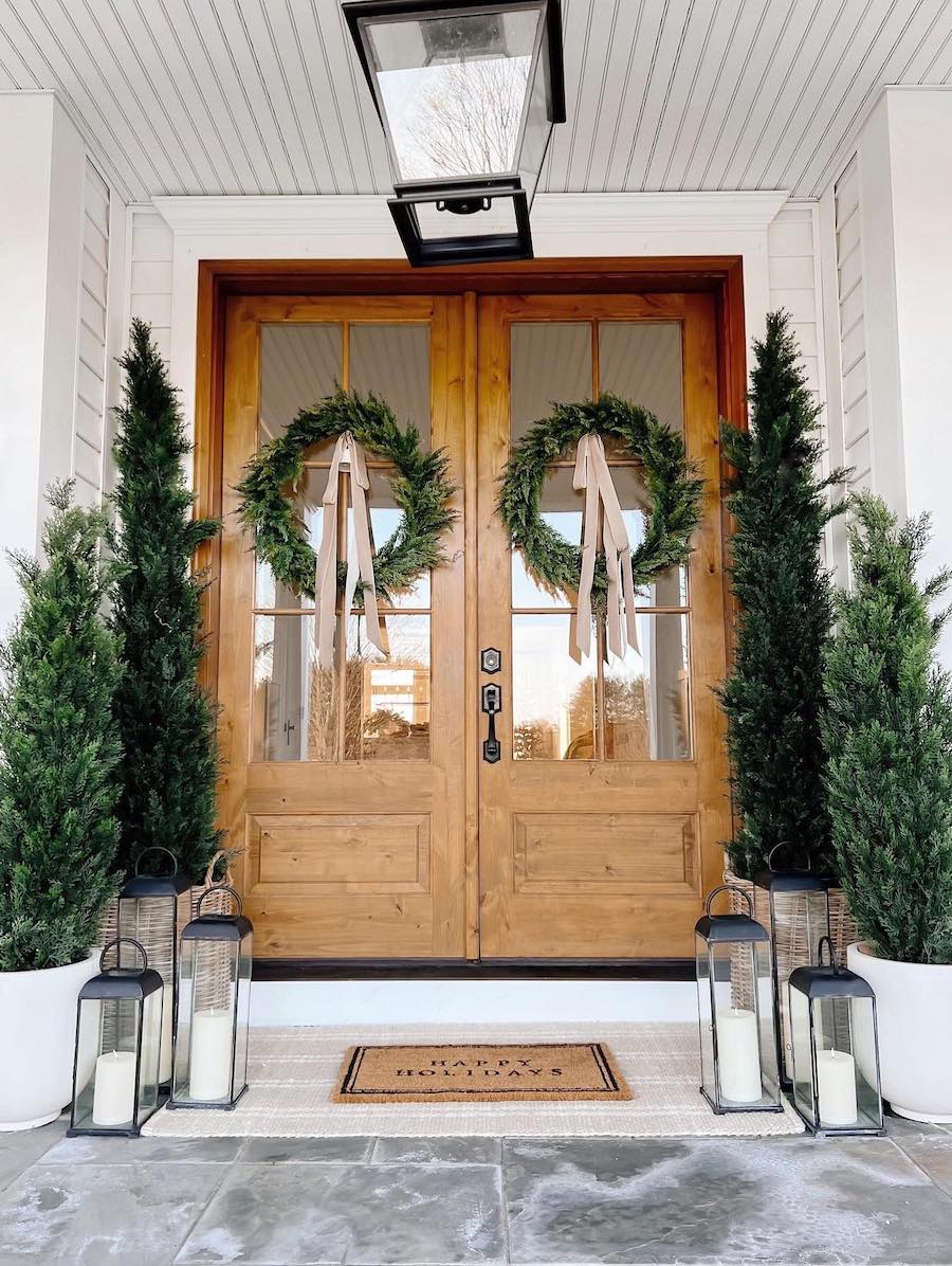 a front porch with pine trees, wreaths, and lanterns