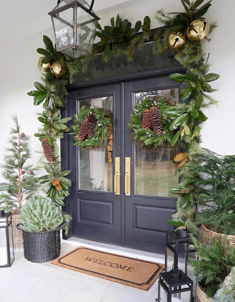 a front porch with outdoor christmas decor including large bells, pine decor, lanterns, and pinecones