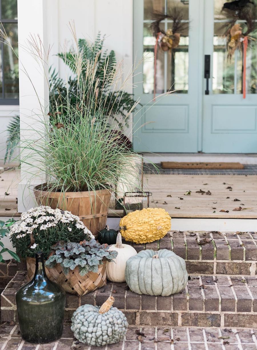 a front porch fall decor display with pumpkins, gourds, and florals