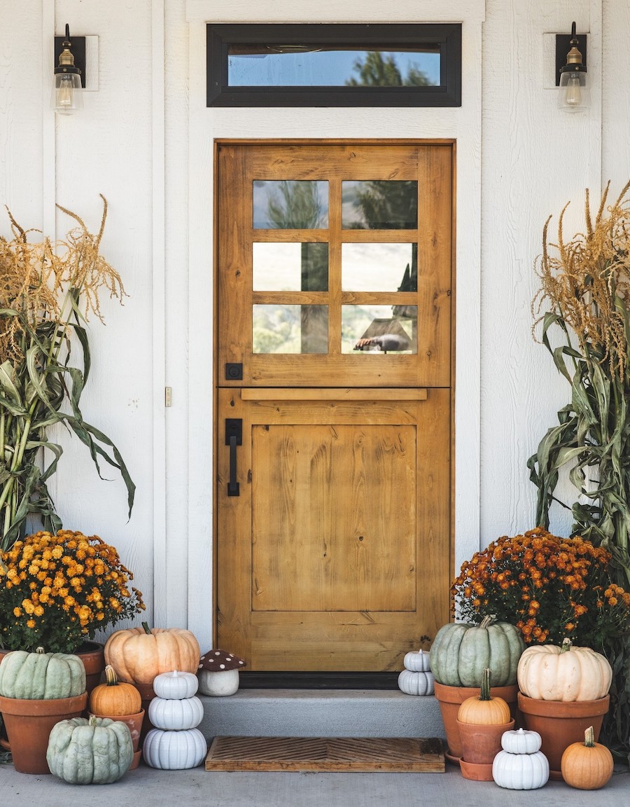 a front porch with stacks of colorful pumpkins, harvest stocks, and florals