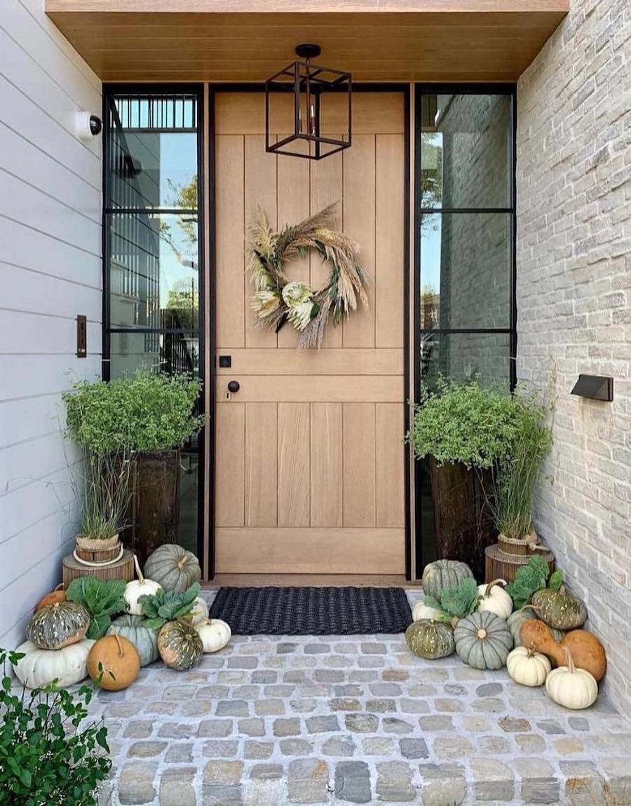 a doorstep with pumpkins, bright green foliage, and a fall-inspired wreath