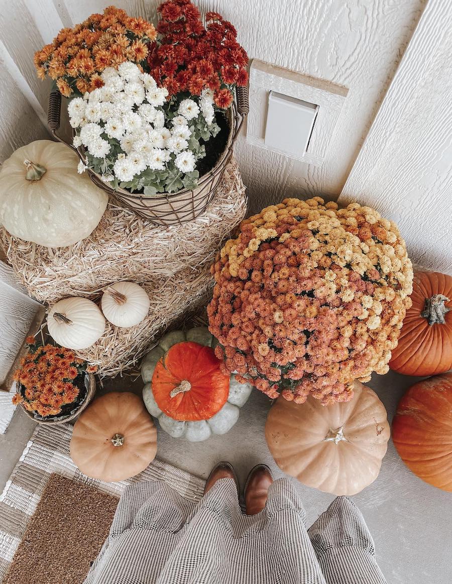 a front porch with hay bales, autumn florals, and colorful pumpkins