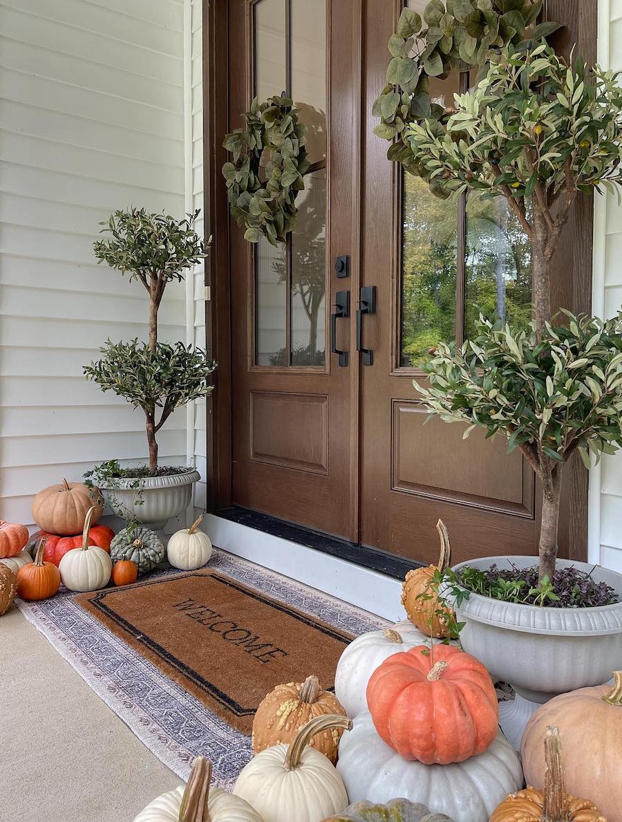 a front porch with piles of pumpkins and plants