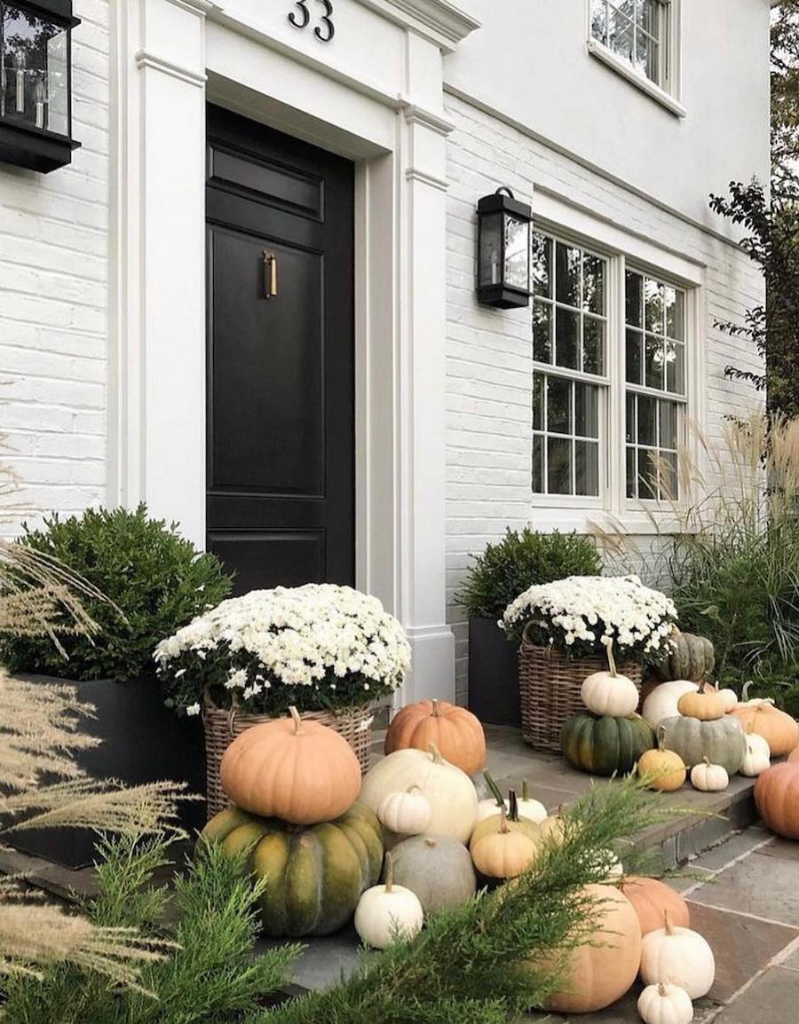 a front porch with piles of pumpkins and white flowers