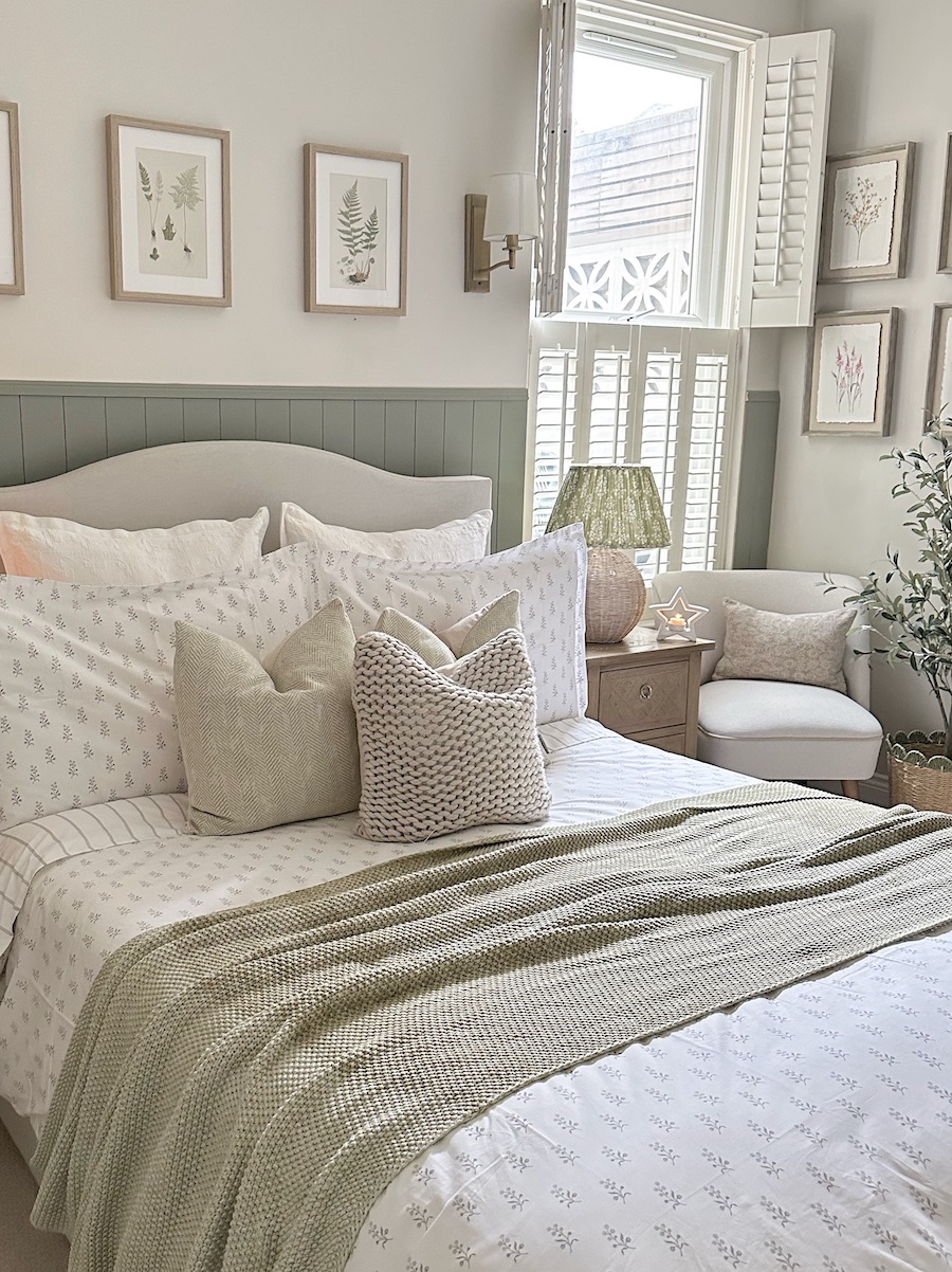 a bright cottage core style bedroom with a sage green accent wall
