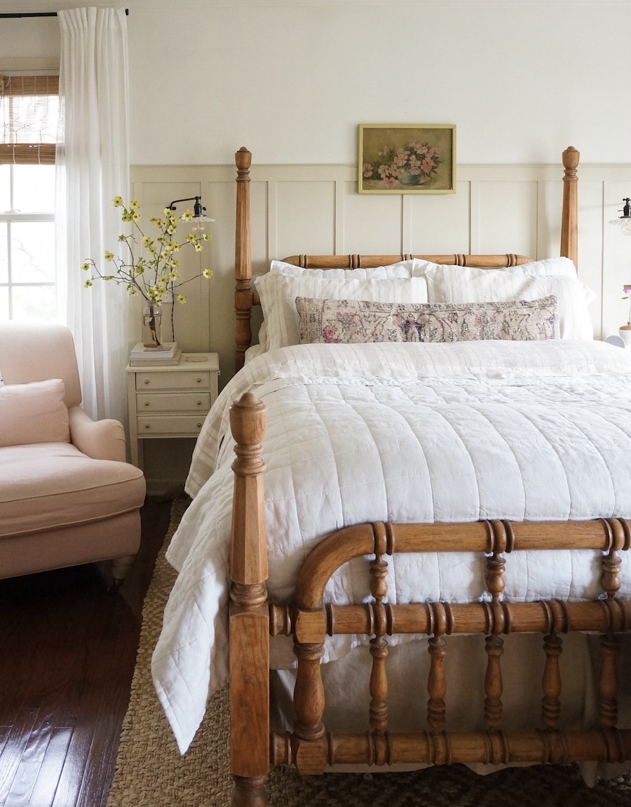 a cottagecore bedroom with warm wood and ivory bedding and floral touches