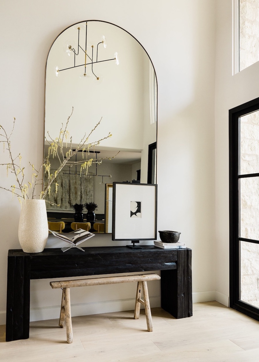 an entryway with a tall rounded mirror and black and white decor