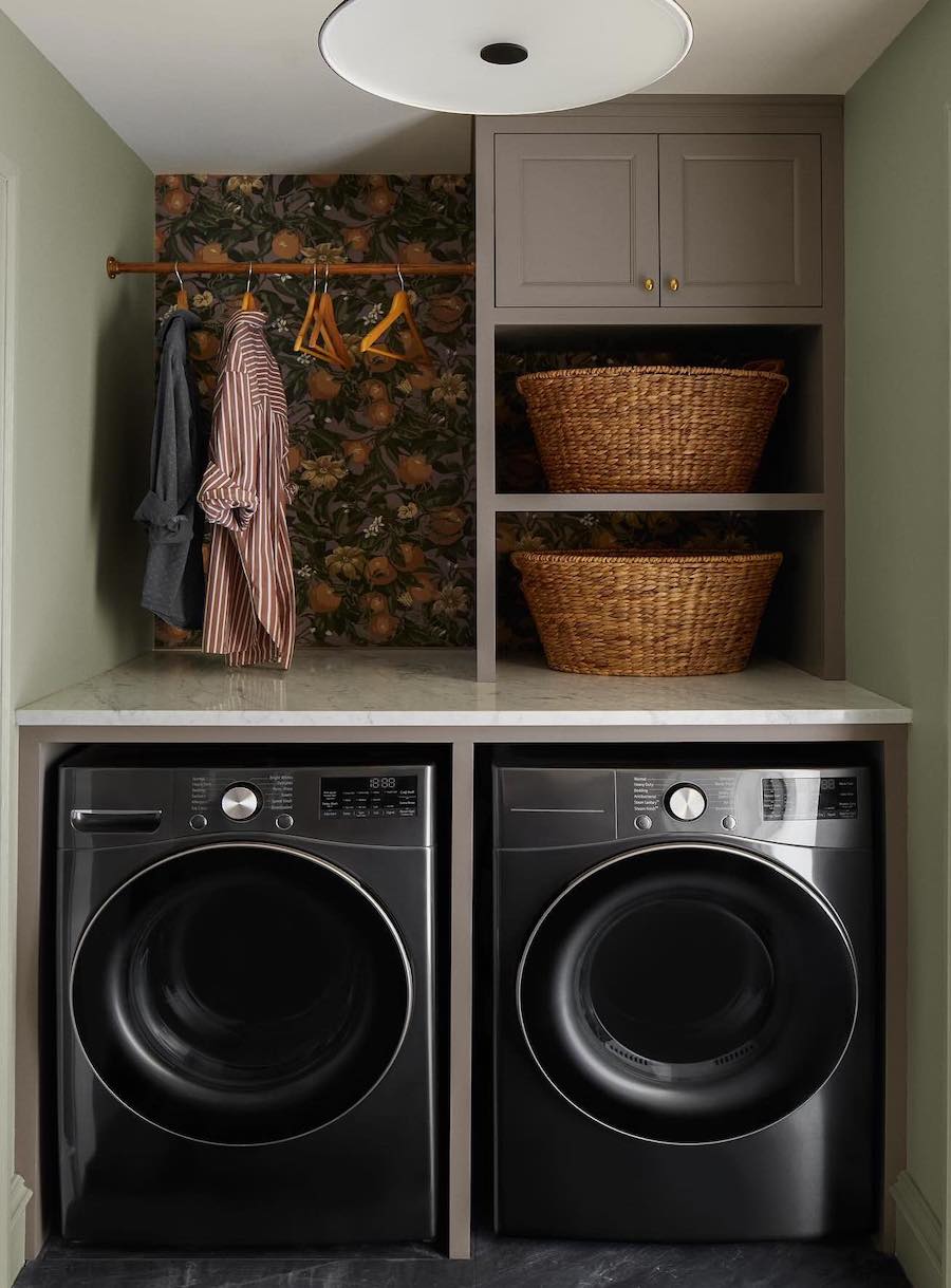 a small laundry room with storage above the machines and wallpaper accents