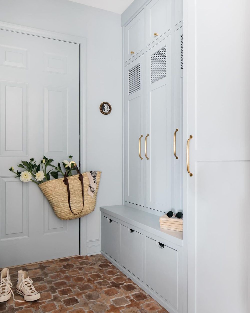 a mudroom featuring a soft blue paint, red brown tiles, gold hardware, and florals