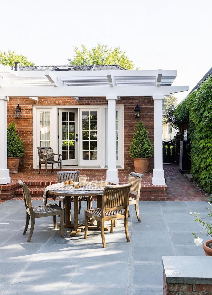 a back porch with a small dining table, brick and a white pergola