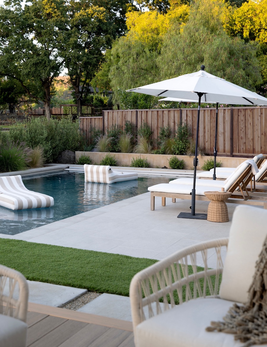 a backyard with lounging chairs and umbrellas, a pool, and other seating