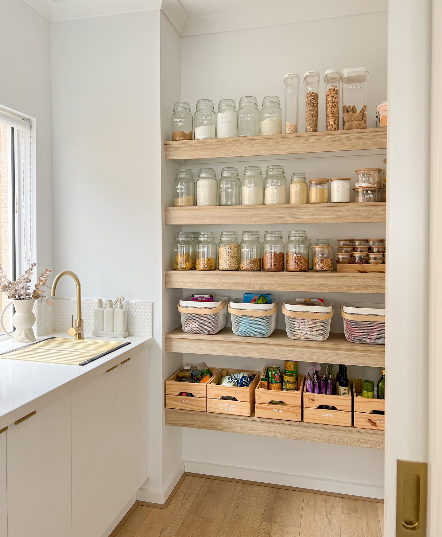 a pantry with built in wooden shelving, glass canisters, and wire and wood baskets and bins