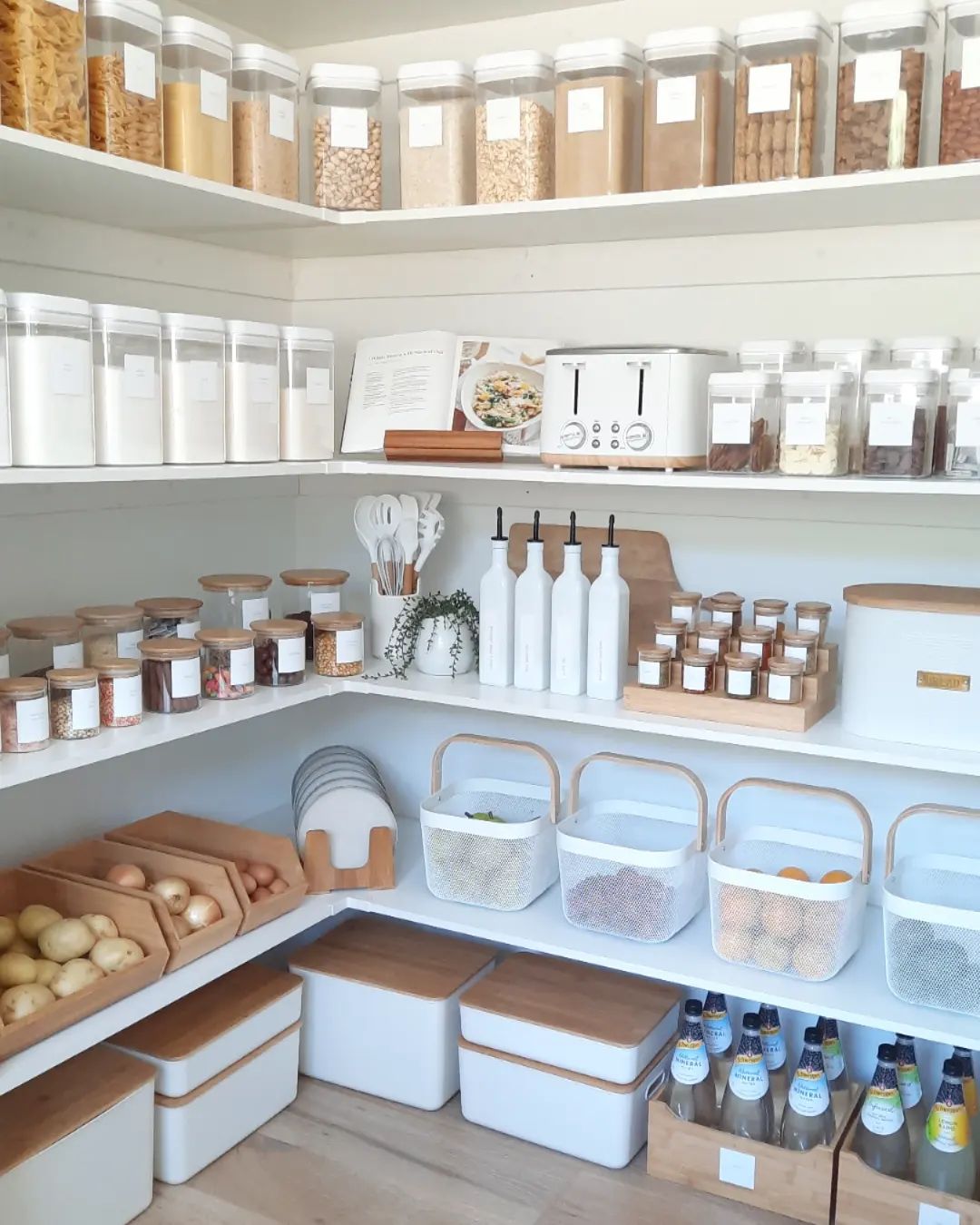 a pantry with white built in shelves, acrylic and glass canisters, wooden bins, and wire baskets